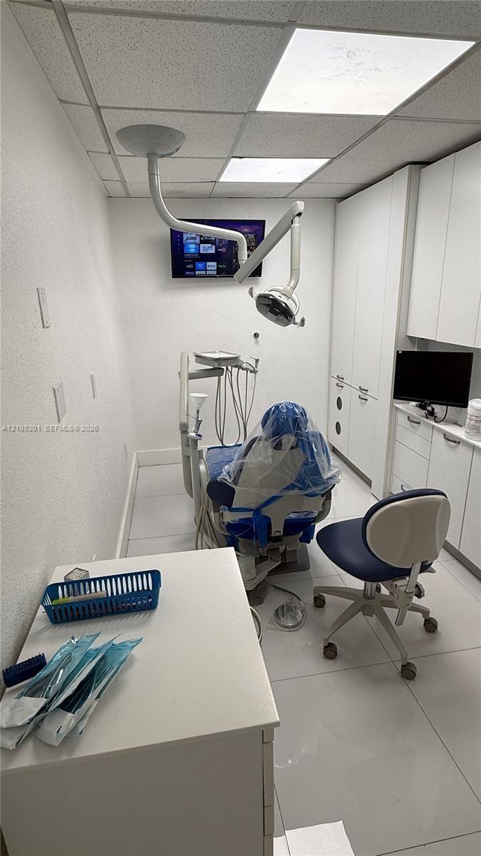 Acoustic tile ceiling with integrated lighting, white walls, built-in cabinetry, and white tile flooring