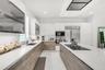 Modern kitchen featuring white glossy and wood-finish cabinetry, white countertops, stainless steel appliances, and an integrated cooktop on the islan