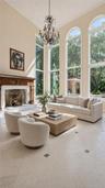High ceilings featuring an ornate chandelier, a fireplace with a carved wood surround, arched windows, and light-toned tile flooring with dark accent 