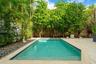 Private swimming pool with integrated steps, surrounded by light-toned decking, a stone perimeter, and lush tropical landscaping