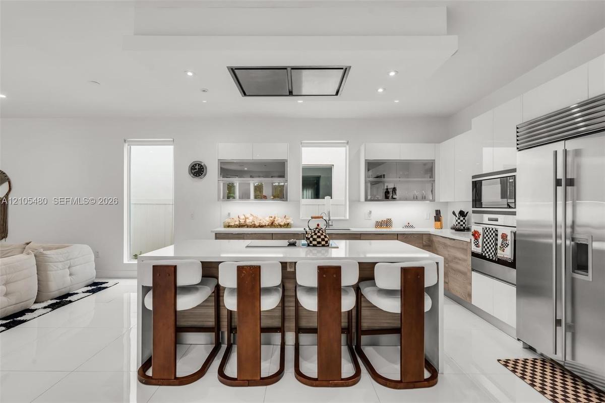 Sleek kitchen featuring a large central island, integrated stainless steel appliances, recessed lighting, and white flooring