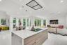 Open-concept living area with white tile flooring, recessed lighting, and a modern island featuring a built-in cooktop and wood-finish cabinetry