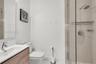 Bathroom featuring a floating wood-finish vanity, integrated rectangular sink, wall-mounted mirror, and a glass-enclosed shower with a rainfall shower