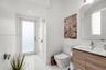 White tile flooring, contemporary vanity with wood-finish cabinetry, rectangular under-mount sink, chrome faucet, and a wall-mounted mirror with integ