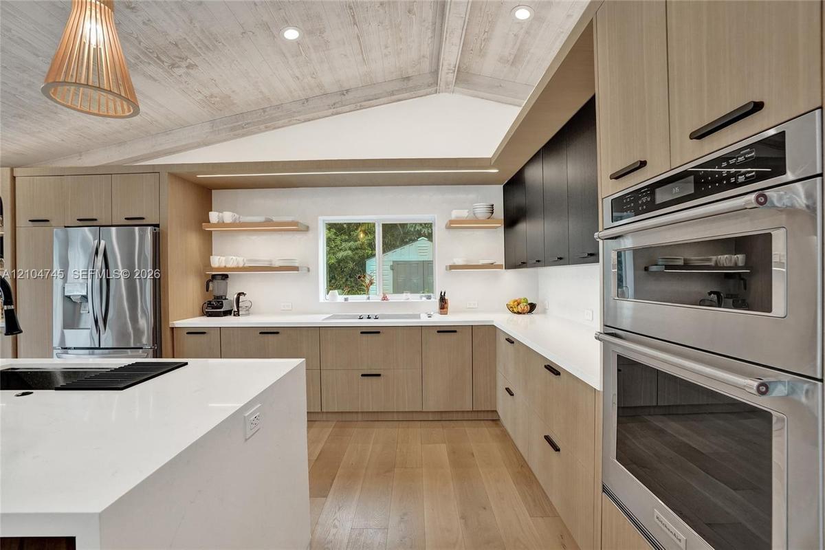 Kitchen with vaulted ceiling, wood-finish beams, stainless steel appliances, white countertops, and wood-finish flooring