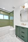 Bathtub with brass-finish fixtures, green subway tile surround, and geometric floor tiling