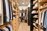Walk-in closet featuring extensive built-in shelving, multiple hanging rods, integrated drawers with dark hardware, and light wood-finish flooring