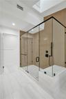 Glass-enclosed shower with matte black fixtures, integrated bench, skylight, and recessed lighting