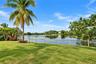 Expansive lawn with a wooden fence bordering a lake, mature palm trees, and established landscaping
