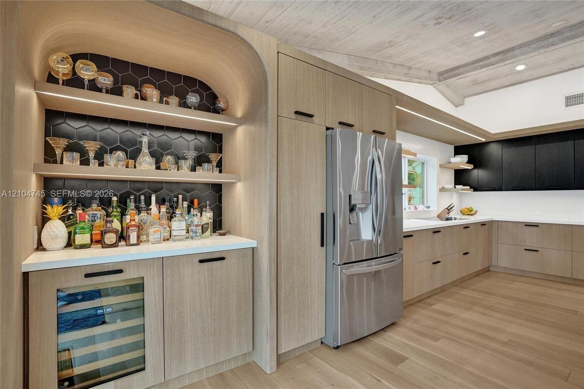 Kitchen featuring light wood-finish flooring, light wood-finish cabinetry, stainless steel refrigerator, white countertops, and a built-in bar area wi