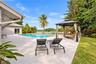 Expansive outdoor patio with a swimming pool, waterfront access, lush landscaping, and a built-in gazebo