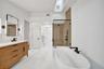 Freestanding soaking tub, frameless glass shower enclosure, wood-finish vanity with countertop, rectangular mirror, and a skylight