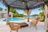 Open-air gazebo with integrated lighting and privacy drapes, expansive patio with a rectangular swimming pool, and solar panels on the roof