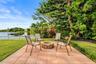 Paver patio with a stone fire pit, bordered by green lawn and diverse foliage, with a water feature in the background