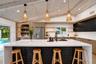 Vaulted wood-finish ceiling, large center island with hexagonal tile accent, built-in stainless steel refrigerator, integrated bar area with shelving,