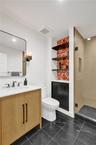 Black tile flooring, single vanity with wood-finish cabinetry, white countertop, modern wall sconce, and a glass-enclosed shower