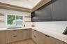 Modern kitchen featuring wood-finish lower cabinetry, dark-finish upper cabinetry, white countertops, and a white hexagonal tile backsplash