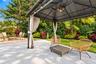 Spacious patio featuring a gazebo with integrated lighting and ceiling fan, a separate paver-stone area with a fire pit, and lush, mature landscaping