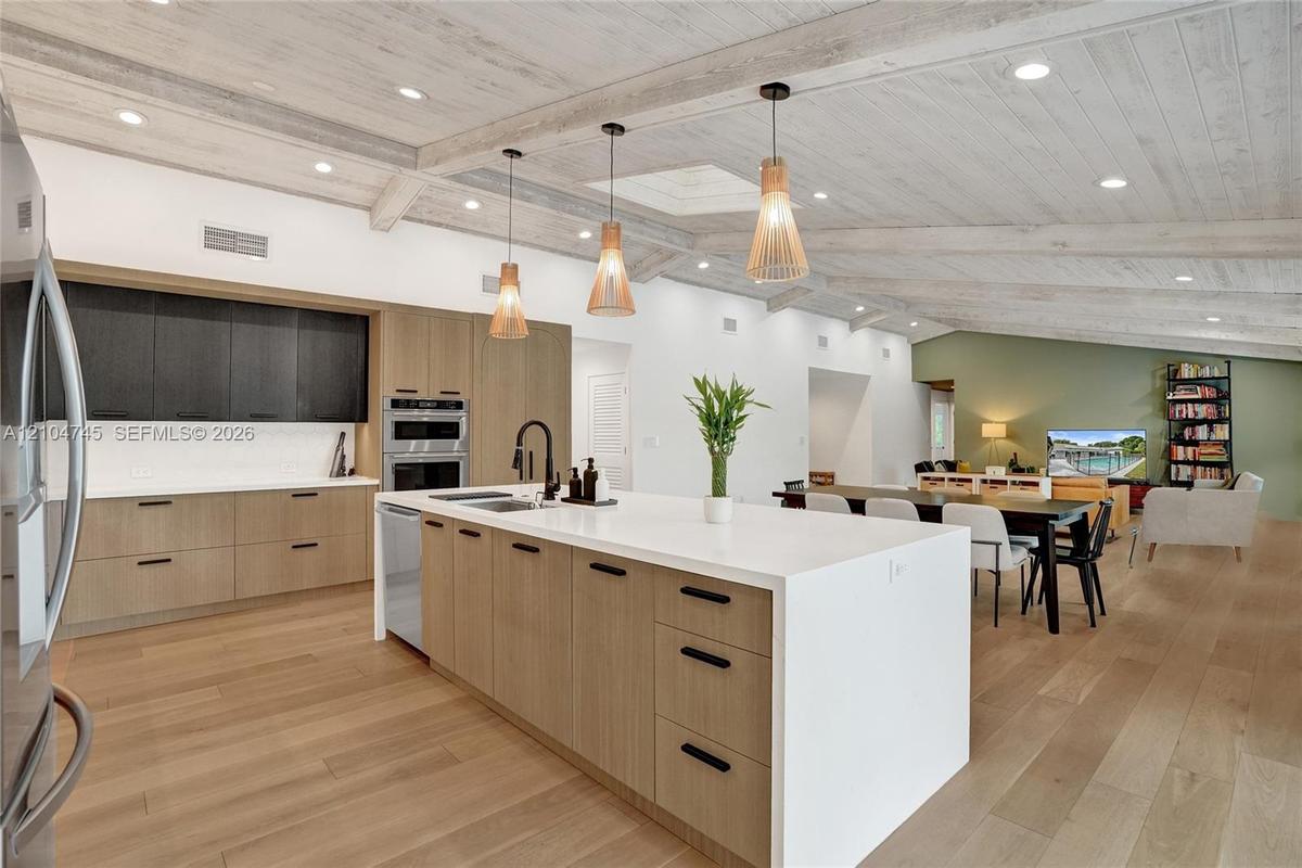 Open-concept kitchen featuring an expansive island with a white countertop, wood-finish cabinetry, and built-in stainless steel appliances