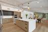 Open-concept kitchen featuring an expansive island with a white countertop, wood-finish cabinetry, and built-in stainless steel appliances