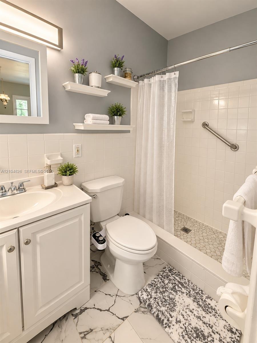 White tile wainscoting and bath surround, white vanity with integrated sink, floating wall shelving, white subway tile shower, and a pebble tile showe