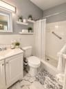 White tile wainscoting and bath surround, white vanity with integrated sink, floating wall shelving, white subway tile shower, and a pebble tile showe
