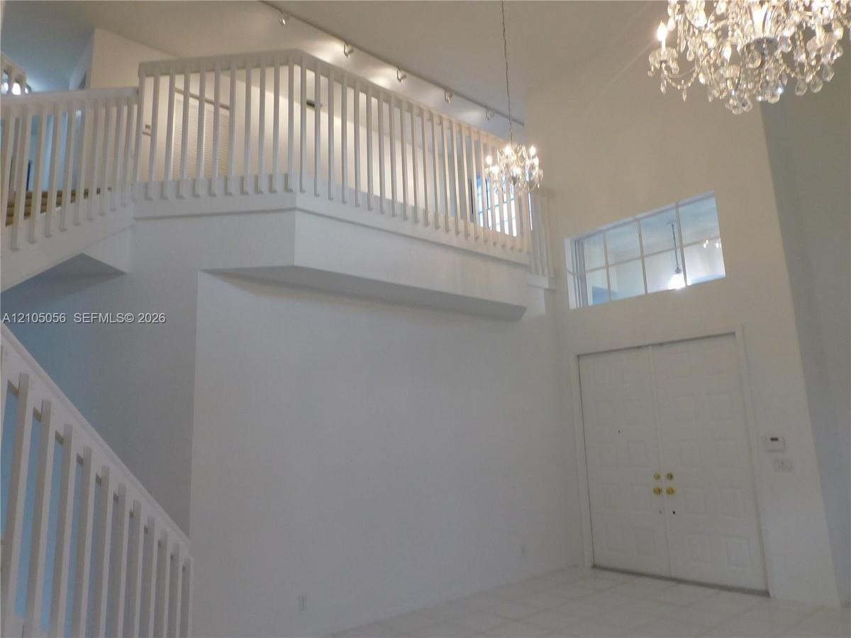 Two-story foyer featuring a double staircase with white balusters, two crystal chandeliers, and loft overlooks social areas - loft is an added bonus t