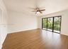 Wood-finish flooring throughout, louvered bi-fold closet doors, ceiling fan with integrated lighting, and sliding glass doors to a balcony with metal 