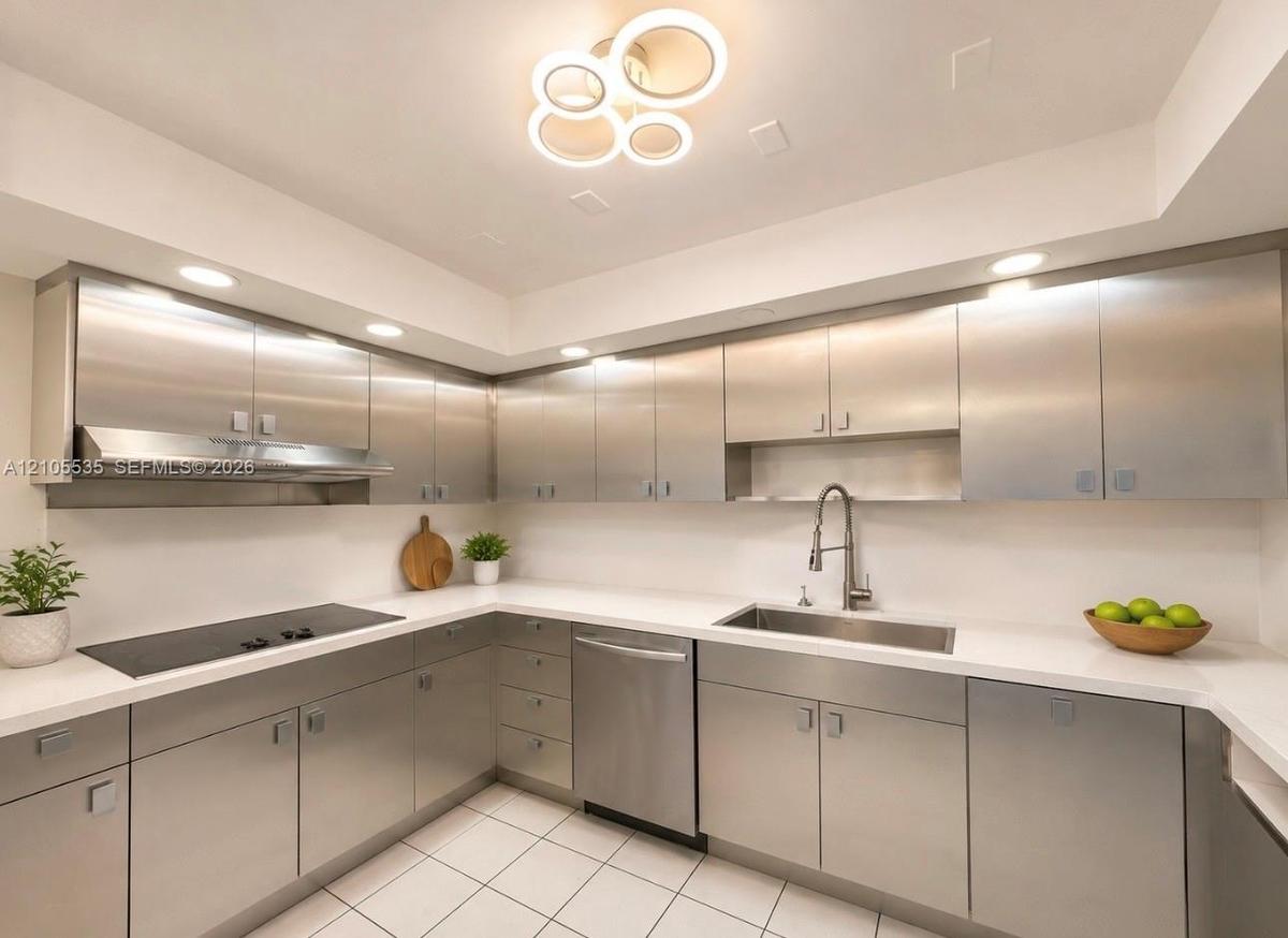 Contemporary kitchen featuring stainless steel cabinetry, white countertops, integrated cooktop, stainless steel range hood, and a modern ceiling ligh