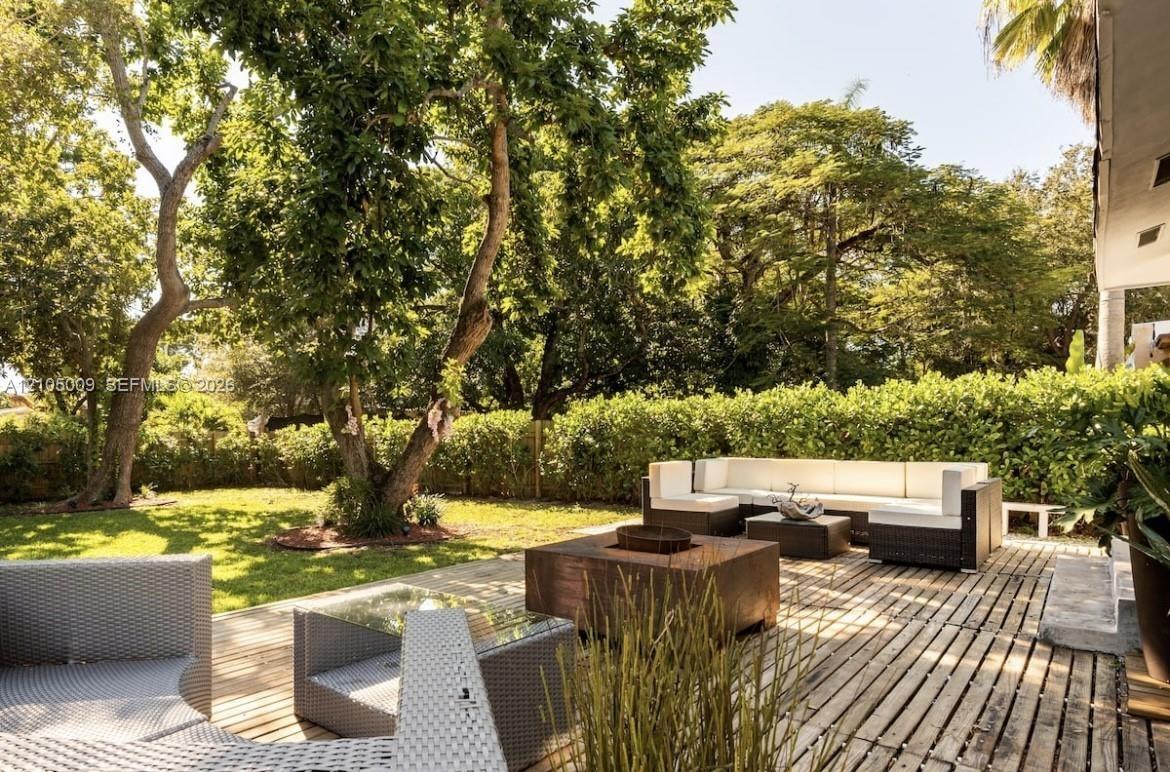 Expansive backyard featuring a manicured lawn, mature trees, and a spacious wood-slat patio