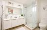 Dual sink vanity with white cabinetry and integrated sinks, large mirrored wall, glass-enclosed shower with tiled walls and floor, and wood-finish flo