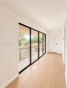Recessed lighting, wood-finish flooring, white paneled walls, white paneled door with black hardware, and multi-panel sliding glass doors accessing an