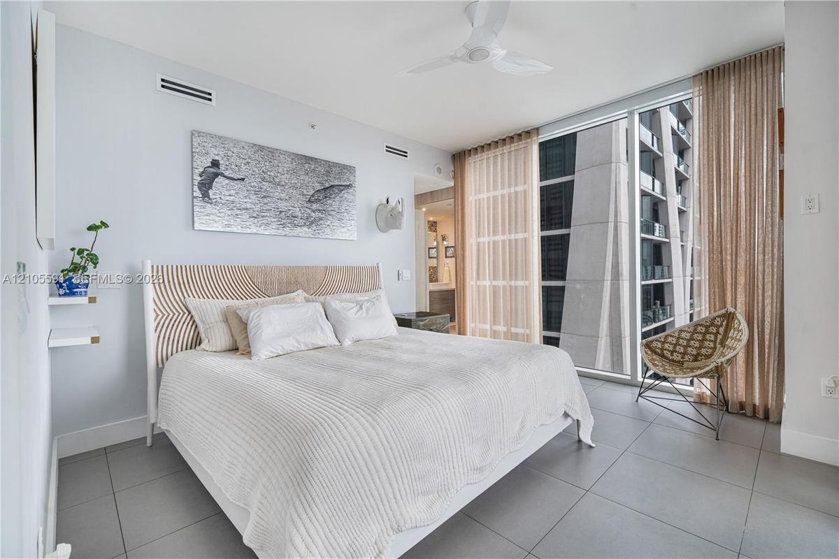 Full-height window with sheer and blackout drapery, ceiling fan, and tile flooring