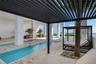 Outdoor amenity area with a louvered pergola, multiple pools, and extensive stone tile decking