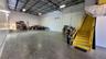 Expansive concrete flooring with a high exposed ceiling, ample overhead lighting, and a prominent yellow staircase with handrails