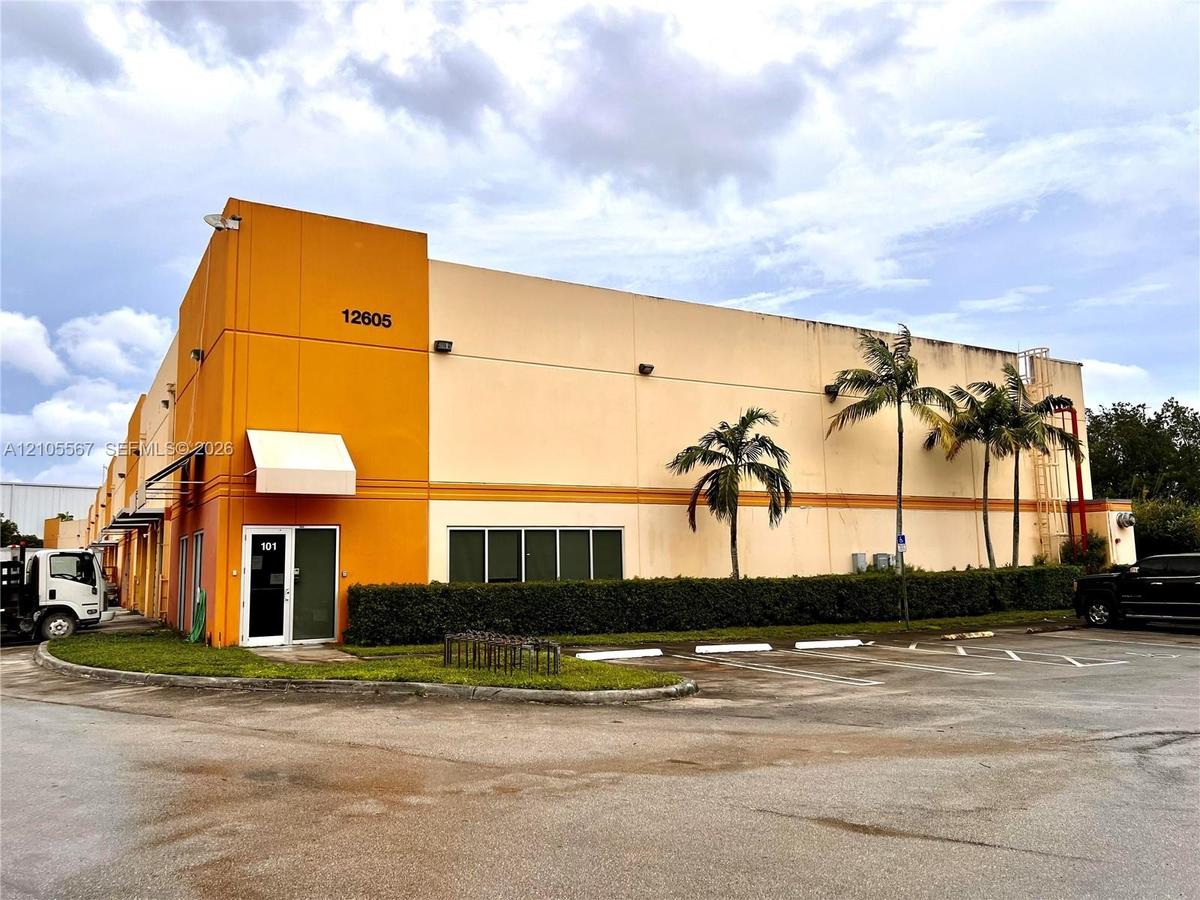 Two-story commercial building with an orange and beige exterior, featuring multiple windows, a white awning, and a paved parking area