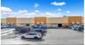 Large paved parking area, commercial building with multiple bay doors, light-colored exterior facade, and exterior awnings