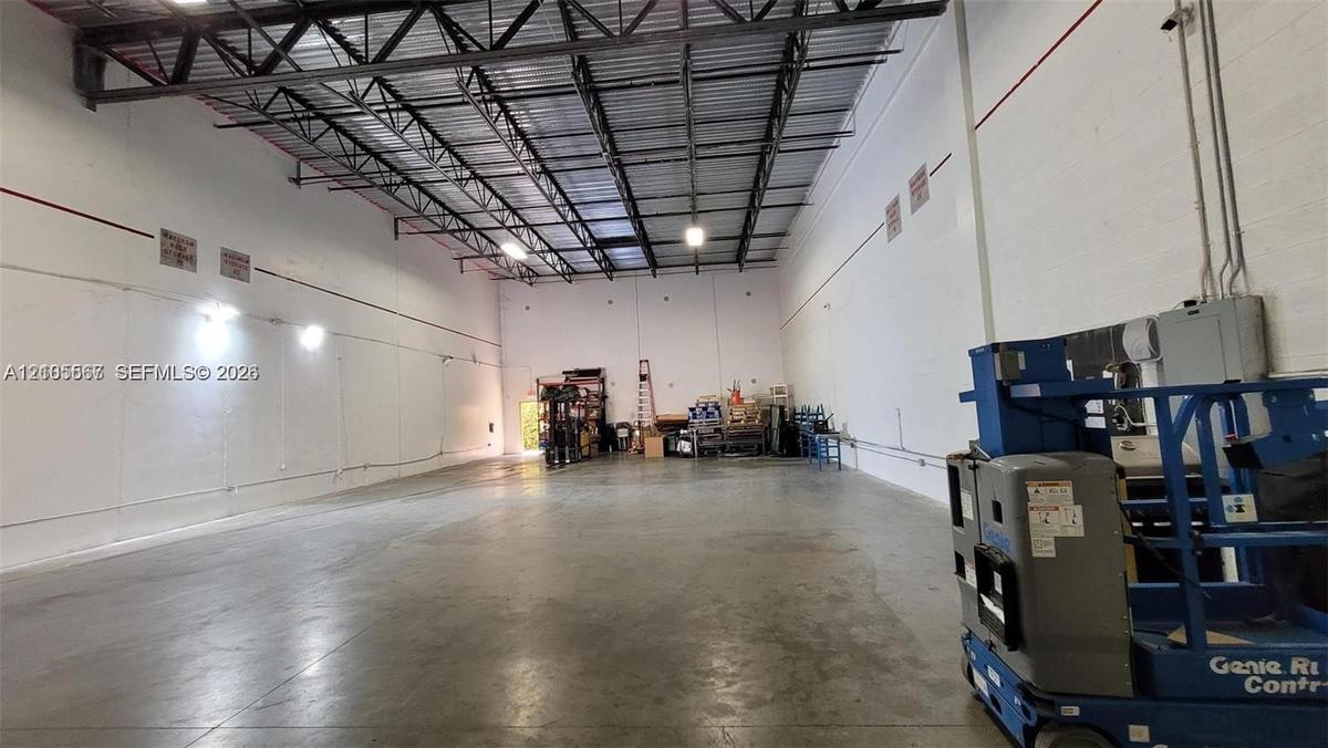 Spacious interior featuring a concrete floor, high exposed metal beam ceiling, white walls, and industrial lighting fixtures