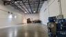 Spacious interior featuring a concrete floor, high exposed metal beam ceiling, white walls, and industrial lighting fixtures