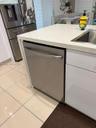 Stainless steel appliances, integrated dishwasher, light-toned tiled flooring, white cabinetry, and a countertop with integrated sink