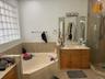 Built-in corner bathtub, glass block window, single vanity with wood cabinetry, large mirror, and glass-enclosed shower