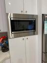 Built-in microwave oven with stainless steel trim, white cabinetry, and light-toned countertop