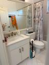 White tiled flooring, vanity with light-colored countertop, undermount sink with brushed nickel faucet, wall-mounted mirror with white frame, and a bu