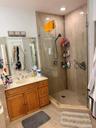 Walk-in shower with glass enclosure, light-toned wall tiling, recessed lighting, and a wood-finish vanity with countertop