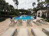 Resort-style pool area featuring a freeform pool, paver deck, lush tropical landscaping, and adjacent cabana structures