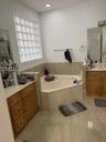 Corner soaking tub with tiled surround, light-colored flooring, and a glass block window