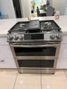 Stainless steel range with a built-in griddle and double ovens, set into a light-toned countertop, complemented by white cabinetry and tile flooring