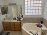 Built-in soaking tub with a tiled surround, glass block window, and an extended vanity with an integrated sink and base cabinetry