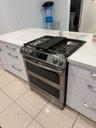 Stainless steel range with double oven, gas cooktop, white cabinetry, integrated drawer pulls, and light-toned countertops