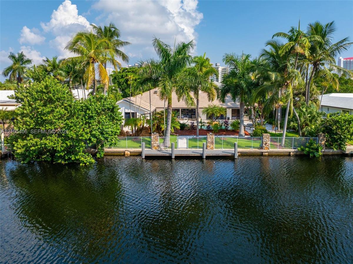 Waterfront property featuring a private dock with pilings, a manicured lawn, mature palm trees, and established landscaping